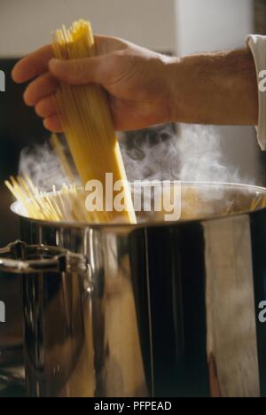 Mano d'uomo immissione spaghetti in padella di cottura a vapore Foto Stock