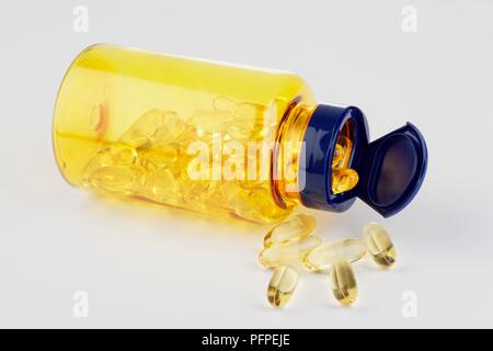 Olio di fegato di merluzzo capsule fuoriuscita dal giallo e pillola blu bottiglia giacente sul lato Foto Stock