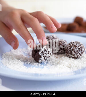 Bambino la laminazione a mano tartufi di cioccolato in scaglie di noci di cocco Foto Stock