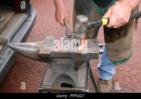 Maniscalco azienda red-metallo caldo a ferro di cavallo con pinze su incudine utilizzando un martello a forma Foto Stock