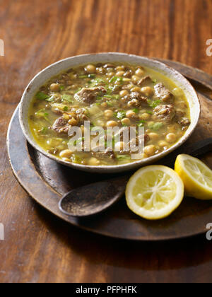 Harira marocchina Zuppa servita nel recipiente rustico sul vassoio sul tavolo con limone spremuto, close-up Foto Stock