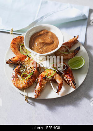 Grigliata di gamberi tigre su spiedini servito sulla piastra con una ciotola di salsa satay Foto Stock