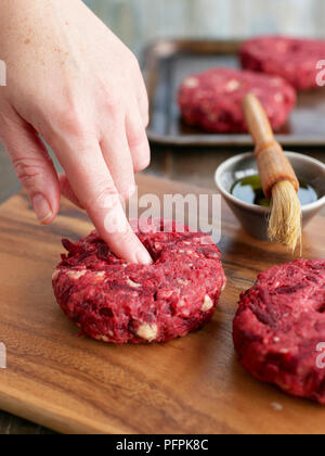 Utilizzando il dito per testare la consistenza della carne di manzo, barbabietole e stilton burger Foto Stock