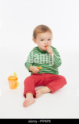 Little Boy in verde stripey top mangiare una carota stick (Modello età - 22 mesi) Foto Stock