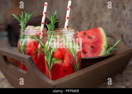 Due vasi di dissetante bevanda estiva con cocomero e rosmarino servita su un vassoio in legno Anguria e rosmarino acqua infusa con ghiaccio. Concetto di h Foto Stock