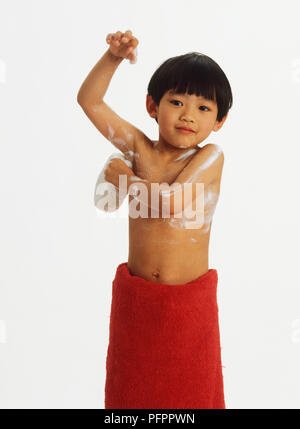 Pulizia del ragazzo se stesso con una spugna e asciugamano rosso avvolto intorno alla vita Foto Stock