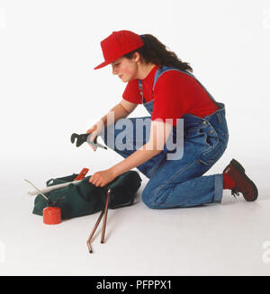 Donna inginocchiato accanto a un kit di utensili, tenere una chiave Foto Stock