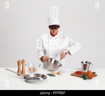 La donna a chef's bianchi sbattere le uova in una terrina Foto Stock