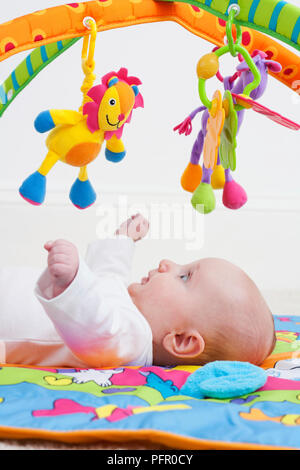 Il Bambino giacente su indietro e guardare fino a giocattoli appeso dal telaio Foto Stock