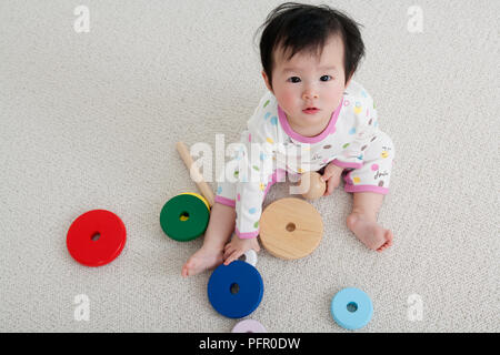 Baby ragazza seduta sul pavimento con i giocattoli di legno, guardando verso l'alto Foto Stock