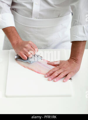 La scuoiatura una sogliola di Dover, tirando la pelle lentamente verso la testa Foto Stock