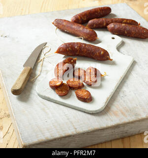 Intero e affettato Chorizo sul tagliere con un piccolo coltello da cucina Foto Stock