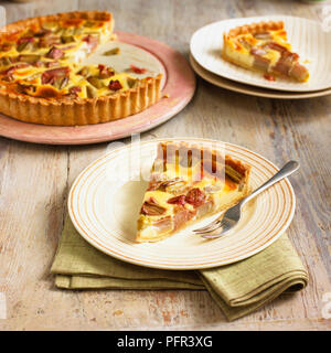 Fetta di rabarbaro e crema pasticcera tart sulla piastra, con forcella, un altro strato e il resto della crostata in background Foto Stock