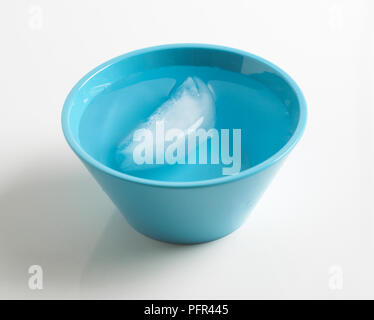 Il cubo di ghiaccio galleggiante nella ciotola blu di acqua Foto Stock