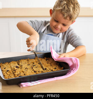 Ragazzo di taglio barre muesli in un vassoio, 4 anni Foto Stock