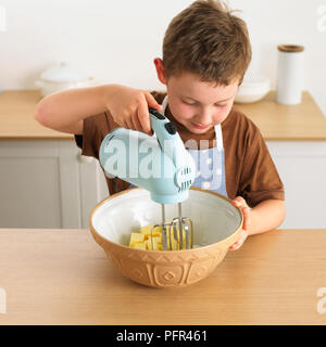 Ragazzo terrina di burro e lo zucchero con un mixer elettrico, facendo una torta, 8 anni Foto Stock