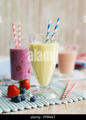 Occhiali con cannucce potabile contenente vari frullati di frutta, le banane e il mango in primo piano e, fragola e mirtillo ulteriormente indietro Foto Stock