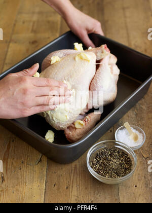 Strofinando il burro sul pollo crudo in teglia Foto Stock