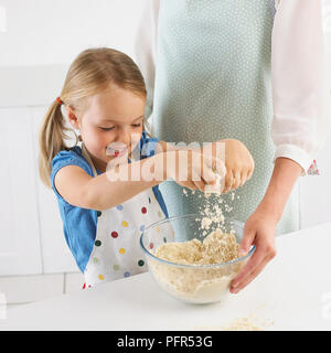 Ragazza strofinando la farina e il burro insieme per far sì che la pasta biscotto, 5 anni Foto Stock