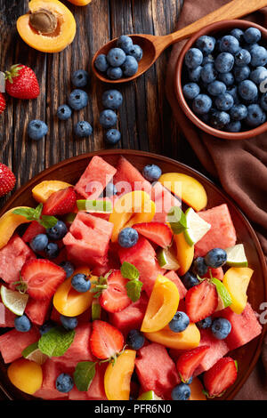 Deliziosa colorata frutta fresca e bacche con insalata di anguria, mirtilli, pesche tagliate a fette, fragola e calce su una piastra su un tavolo di legno con ingre Foto Stock