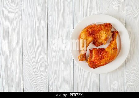 Fritti croccanti le cosce di pollo su una piastra bianca su una tavola di legno, piatto laico, vista da sopra Foto Stock