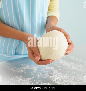 La ragazza mani tenendo palla di pasta di pane al di sopra del piano di lavoro infarinata, close-up Foto Stock