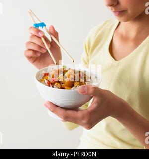 Ragazza con una ciotola di dolce e aspro la carne di maiale in una mano e bastoncini nell'altra mano, close-up Foto Stock