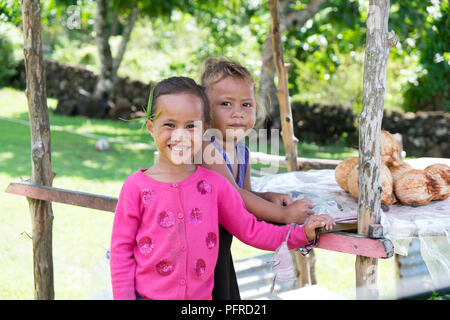 Savai'i Island, Samoa - Agosto 1, 2018: Cute ragazze vendita di noci di cocco fresco sulla pressione di stallo dal lato della strada Foto Stock