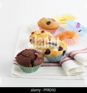 Una selezione di muffin su un canovaccio, compresi chocolate chip muffin, muffin ai mirtilli, cranberry muffin, raisin muffin, e casi di carta Foto Stock