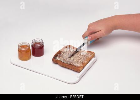 Donna che utilizza il coltello con la mano destro afferrare per spalmare il burro sul pane tostato sul vassoio con bordo rialzato per arrestare il movimento di toast Foto Stock