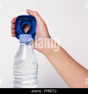 Mano che regge in plastica blu apribottiglie sopra il coperchio della bottiglia di acqua Foto Stock