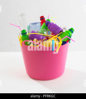 Rosa di plastica paniere pieno di plastica colorata di oggetti quali bottiglie, cannucce e pioli Foto Stock