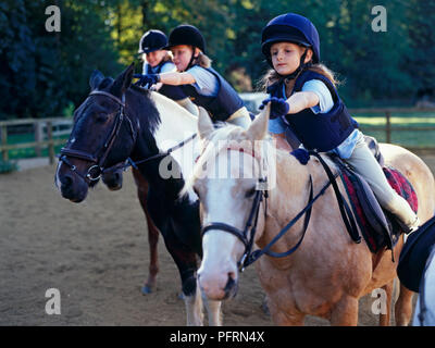 Le tre ragazze sul pony raggiungendo a toccare i pony' orecchie Foto Stock