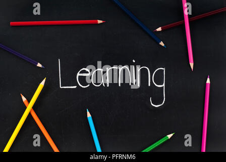 La parola 'apprendimento' scritto in gesso su una lavagna e alcune matite colorate Foto Stock