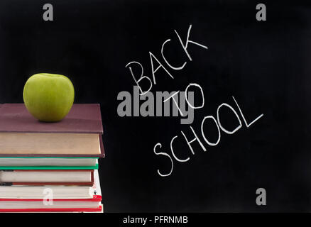 La frase "Si torna a scuola" scritto in gesso su una lavagna, accanto a una pila di libri con un Apple sulla parte superiore Foto Stock