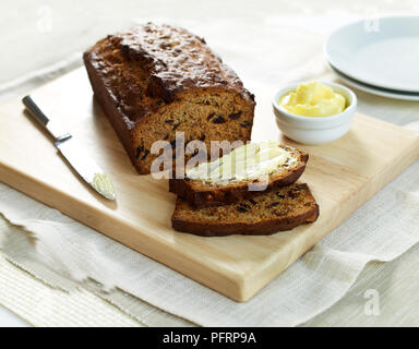 Data di legno di noce e focaccia con alcune fette tagliate via e una delle fette imburrata, coltello e burro nelle vicinanze Foto Stock