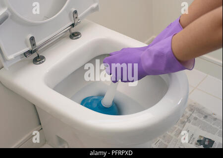 Donna che indossa il viola lavaggio fino un paio di guanti per sbloccare servizi igienici con stantuffo Foto Stock