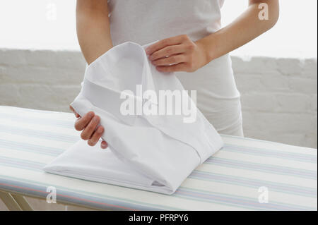 La donna la piegatura stirare una camicia bianca sulla tavola da stiro Foto Stock