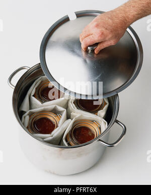 Il trattamento termico delle conserve in vasi di vetro, posizionando il coperchio sulla pentola in acciaio Foto Stock