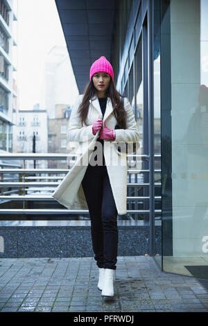 Giovane donna holding camice bianco rosa da indossare guanti e cappello. Foto Stock
