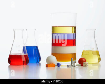 Torre di densità esperimento, vaso trasparente con 5 strati di liquido - miele, latte detergente, acqua (con blue colorante alimentare), e l'olio vegetale, circondato da tavolo palla da tennis, viti di marmo, blocco di lego, dadi e pomodoro ciliegino. Tre vetro extra contenitore incluso, contenenti detersivo, blu acqua e olio vegetale Foto Stock