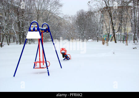 Parco giochi infantile coperte di neve in inverno. Da soli swing sul parco giochi per i bambini durante il ciclone di neve. Cantiere vuoto in città europea dopo snowfal Foto Stock