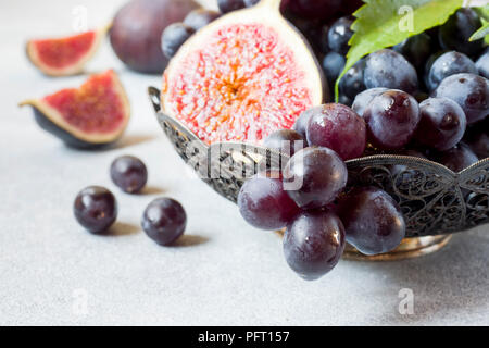 Fichi freschi e uva nera con foglie in una piastra su una tabella grigia messa a fuoco selettiva. Foto Stock