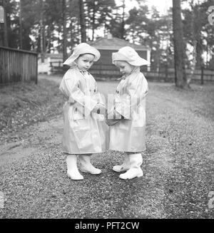 bambini degli anni '1950 in abiti da pioggia. Due bambini sono in piedi fuori in una giornata di pioggia, vestiti con impermeabili e stivali di gomma. Svezia 1952 rif. BH91-11 Foto Stock