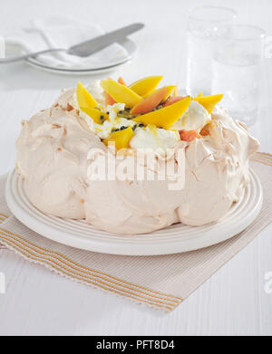 Pavlova guarnita con frutta tropicale e la crema è servita con bicchieri di acqua Foto Stock
