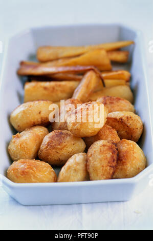 Patate arrosto e pastinache nel piatto di portata sulla tovaglia bianca Foto Stock