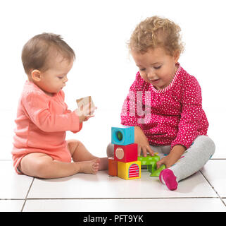 Baby girl (8 mesi) e toddler girl (2 anni) seduto a giocare con i blocchi di costruzione Foto Stock