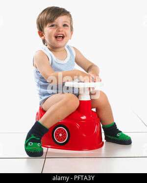 Ragazzo seduto su un vasino conformata come una vettura con il volante, 20 mesi Foto Stock