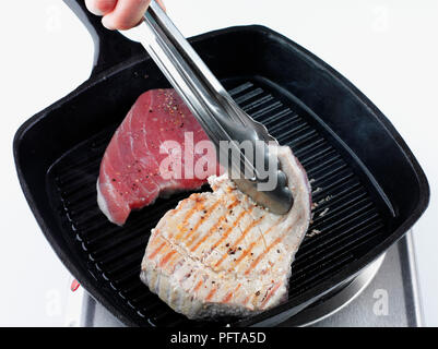Char Grill-filetti di tonno in padella, servendosi di un paio di pinze per capovolgere le bistecche Foto Stock
