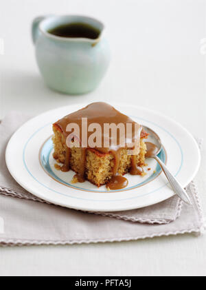 Fetta di sticky toffee pudding con lo zenzero, la brocca di salsa di caramello derivata in background Foto Stock